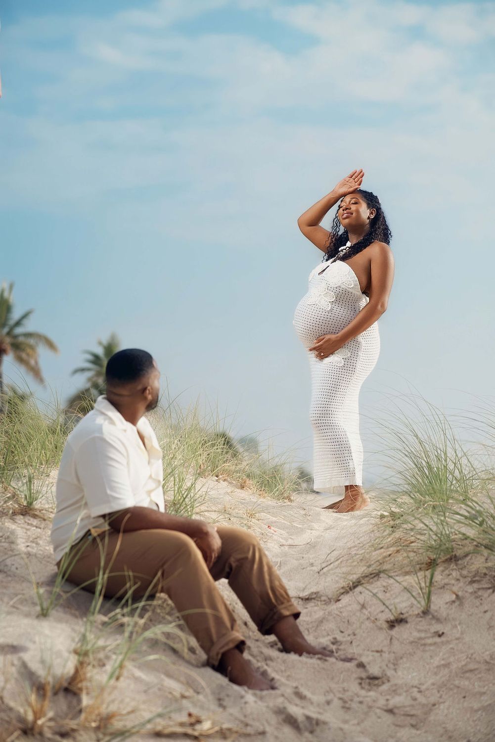 Mother to be standing in the sea oats as her partner watches from the sand