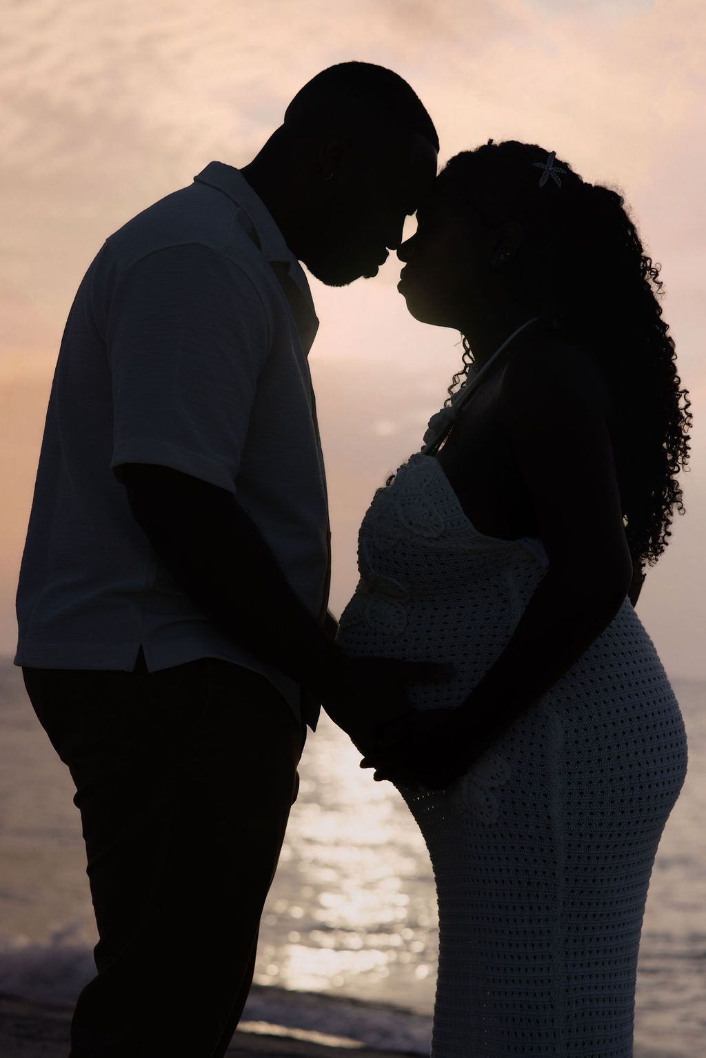 Expecting couple in silhouette against the sunset, her belly between them