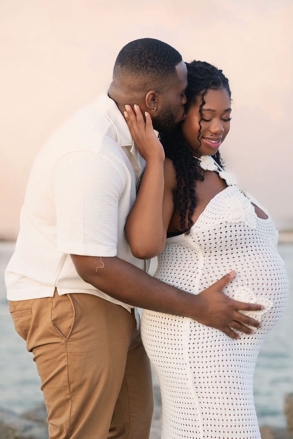 Partner resting his hand on her belly at the beach