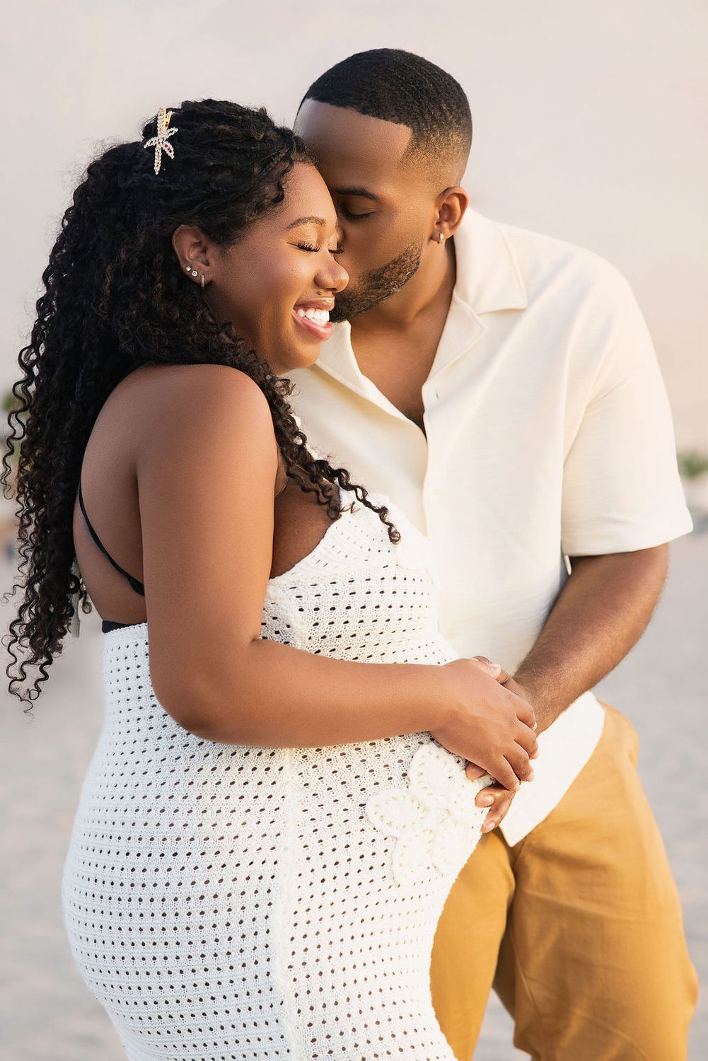 Expecting couple laughing together on the sand at golden hour