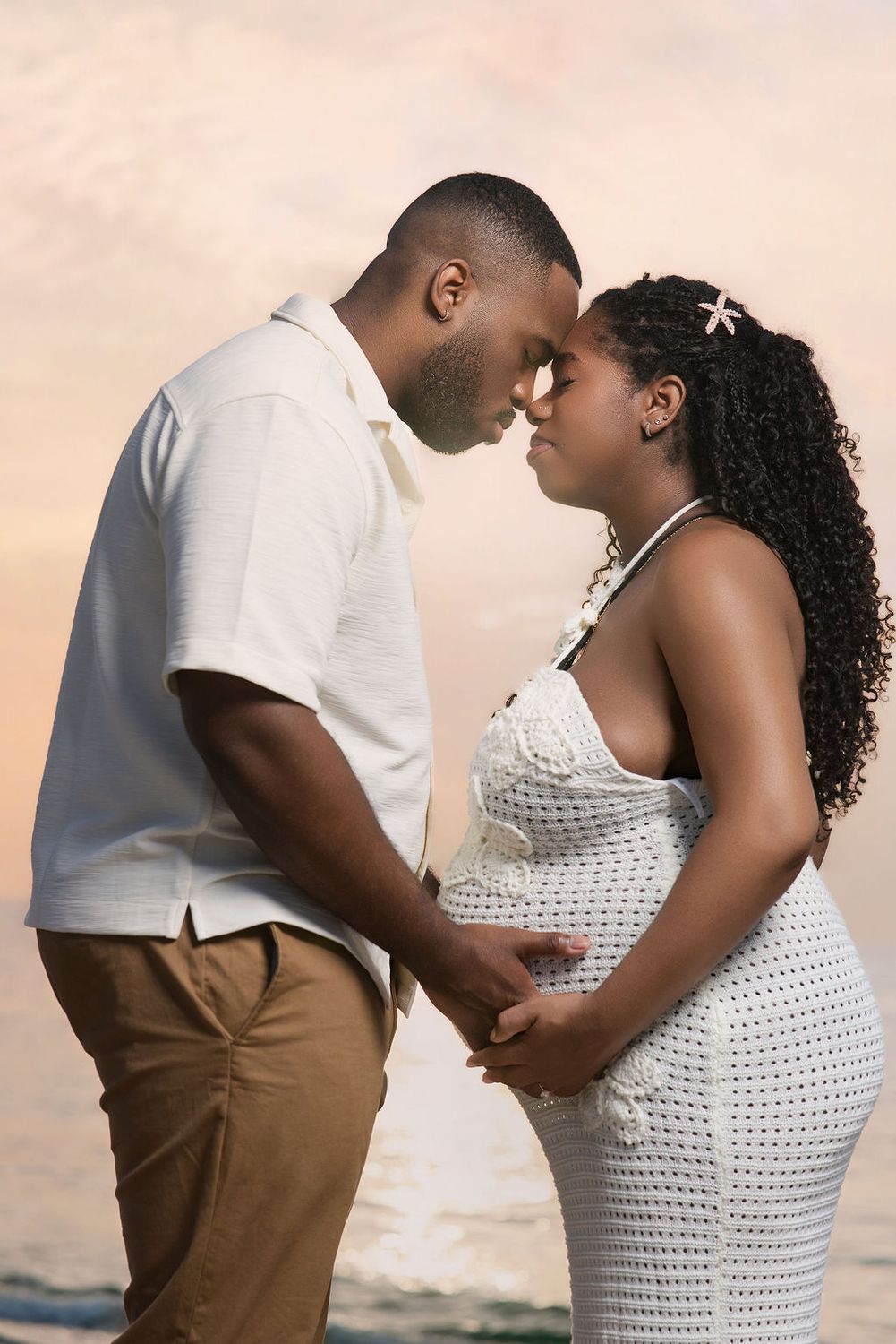 Expecting couple forehead to forehead, both hands on her belly
