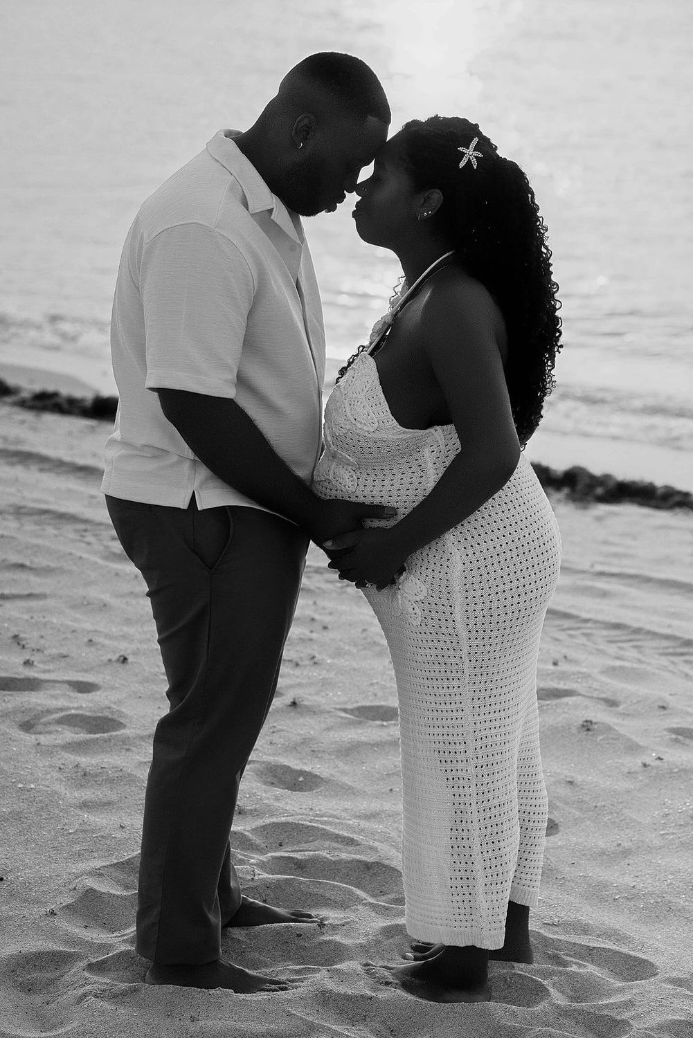Black and white photograph of an expecting couple kissing on the beach
